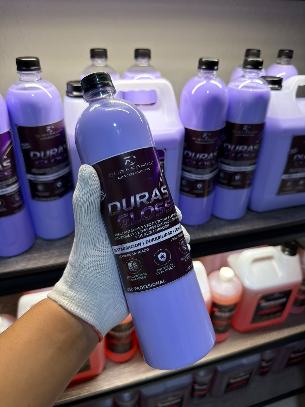 Botella de Duras Gloss de 1 litro en la mano, frente a botellas en la bodega